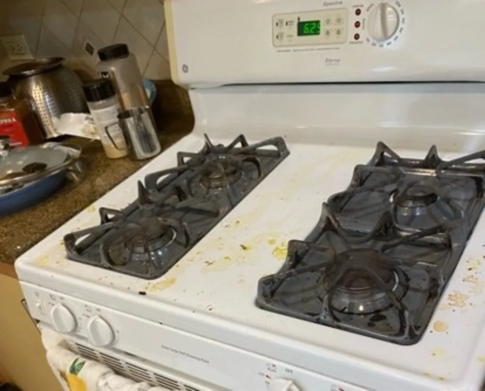 White enamel gas range cooktop with grease splatter and soiled cast grates